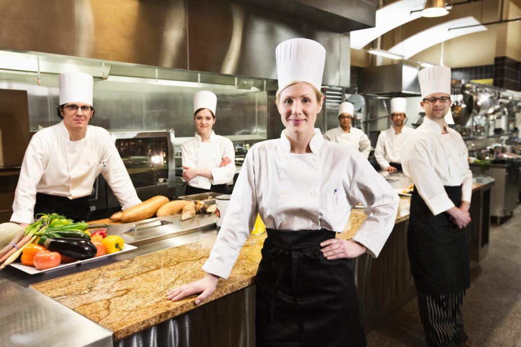 A portrait of a caucasian female chef and her team of chefs in the backgroiund.